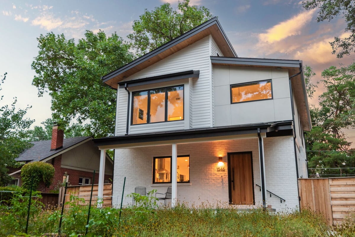 Denver pop top renovation exterior at sunset with sloped roof, white brick, wood door, and native landscaping by Cillessen Construction