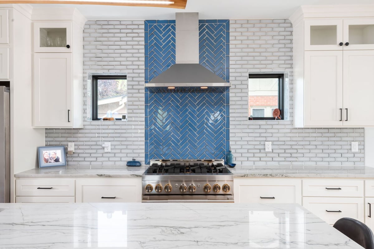 Denver pop top renovation kitchen with blue herringbone backsplash, white cabinets, marble counters, and range hood by Cillessen Construction