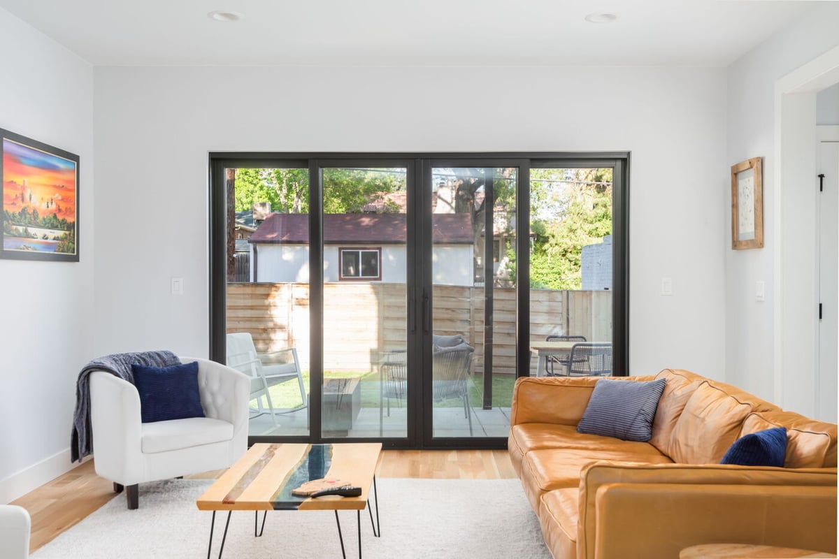 Denver pop top renovation living room with leather sofa, armchairs, and sliding glass doors to patio by Cillessen Construction