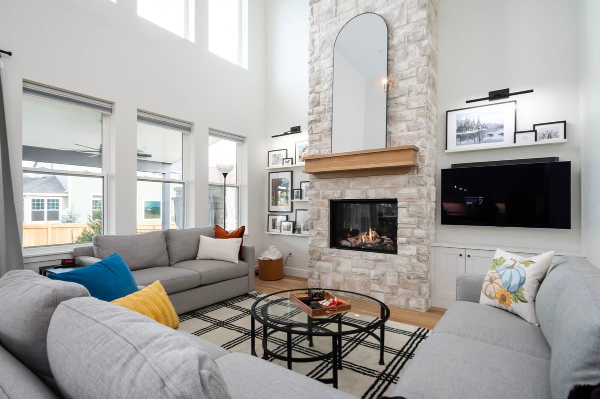 Louisville, CO custom home living room with stone fireplace, tall windows, modern seating, and wall-mounted TV by Cillessen Construction