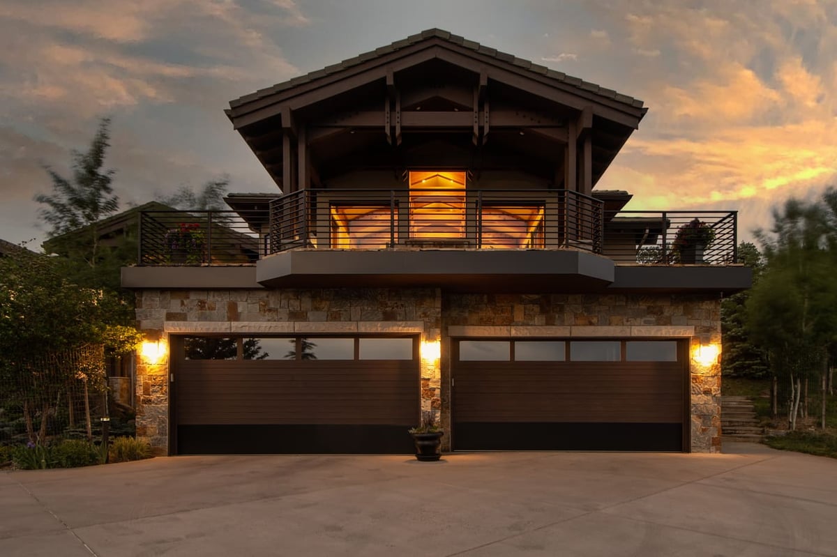Genesee, CO renovation exterior with timber balcony and lit garage at dusk by Cillessen Construction