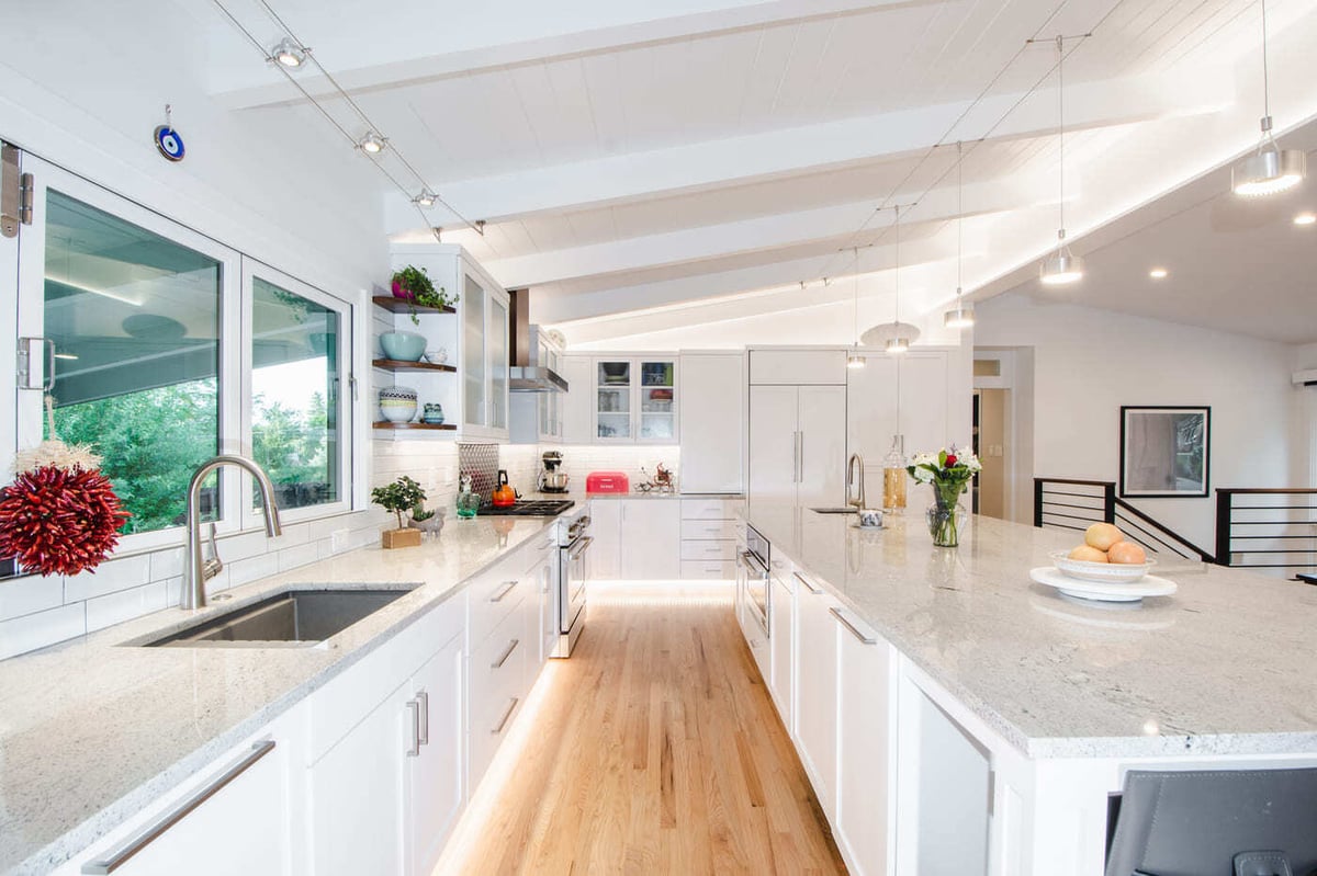 Applewood, CO renovation bright galley kitchen with island, white cabinetry, and large window by Cillessen Construction