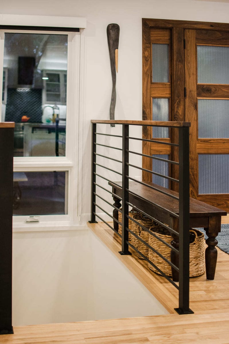 Applewood, CO renovation entry with wood door, black railing, and bench storage by Cillessen Construction