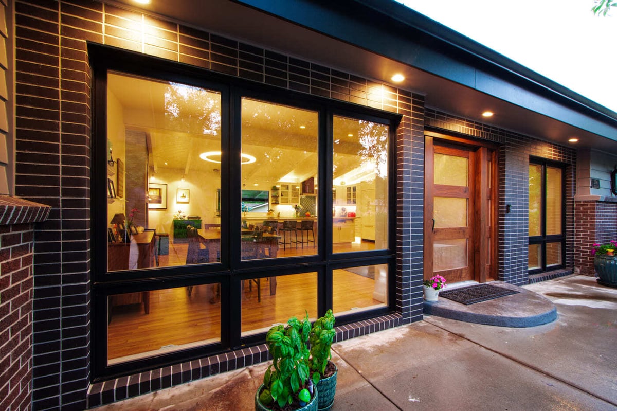 Applewood, CO renovation exterior with large windows, wood door, and patio lighting by Cillessen Construction
