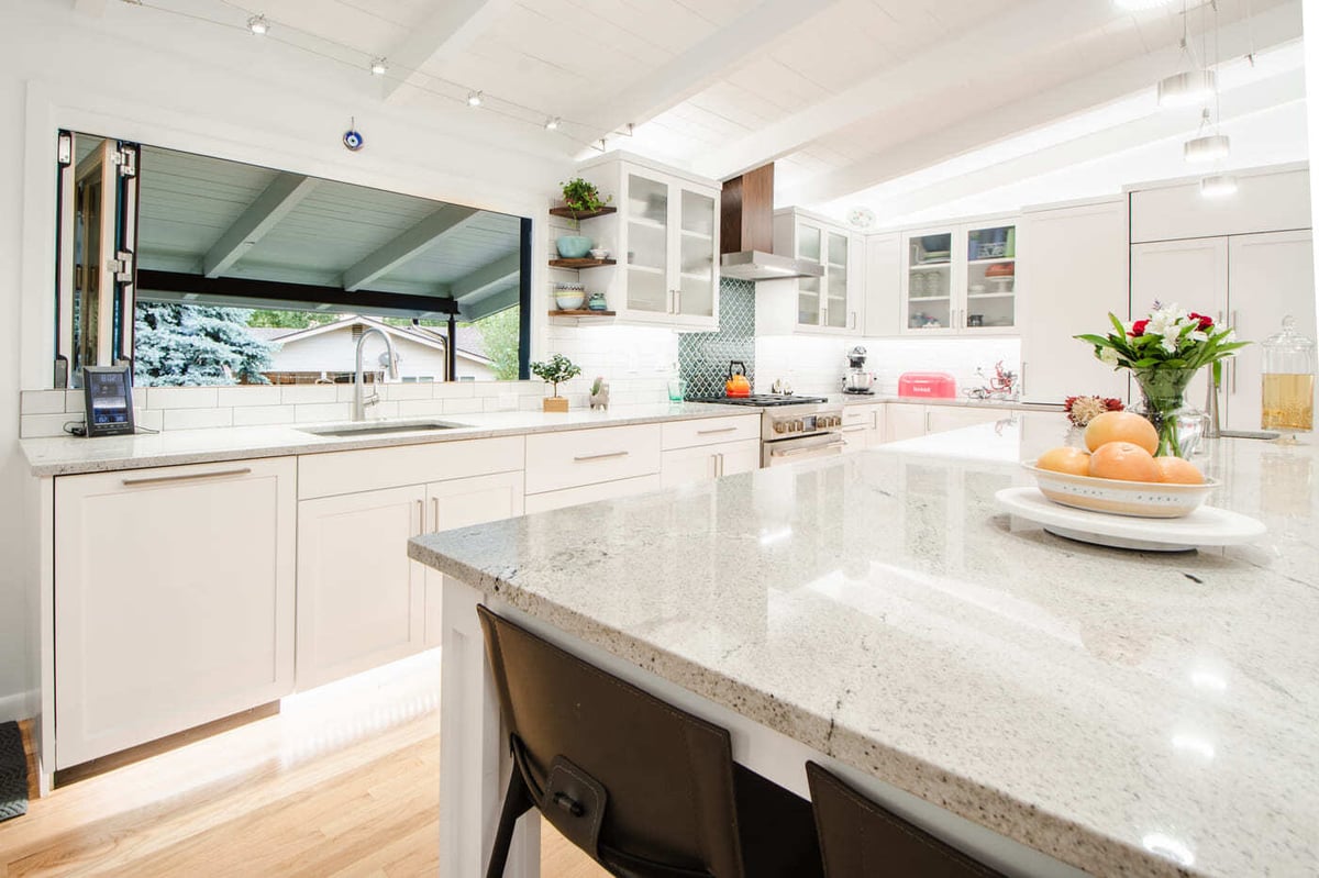 Applewood, CO renovation kitchen with quartz island, white cabinets, tile backsplash, and large pass-through window by Cillessen Construction