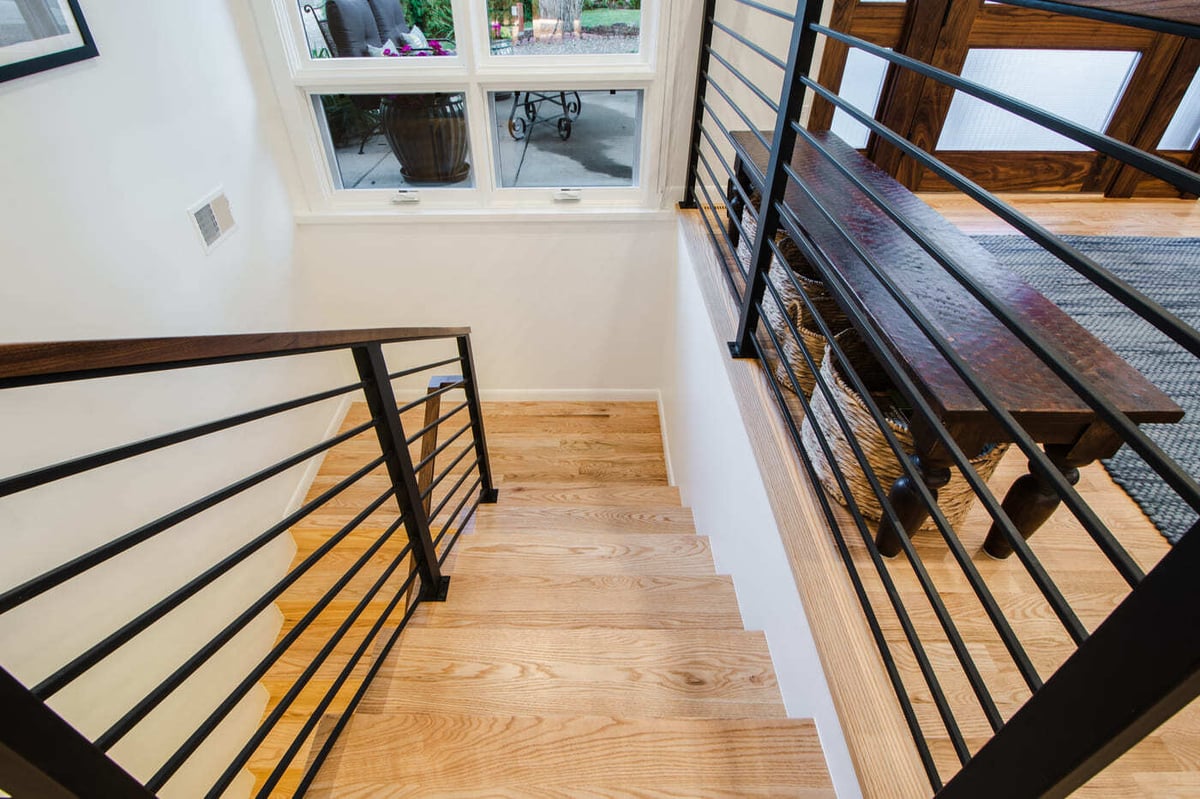 Applewood, CO renovation stair landing with wood treads, black metal railing, and window views by Cillessen Construction