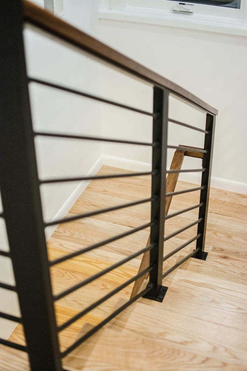 Applewood, CO renovation stair railing detail with wood handrail and black metal balusters by Cillessen Construction