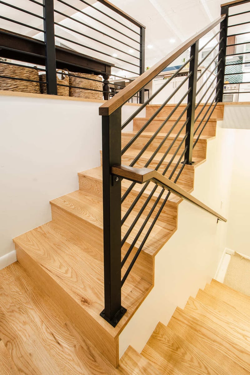 Applewood, CO renovation staircase with wood steps, black metal railing, and open view to kitchen by Cillessen Construction
