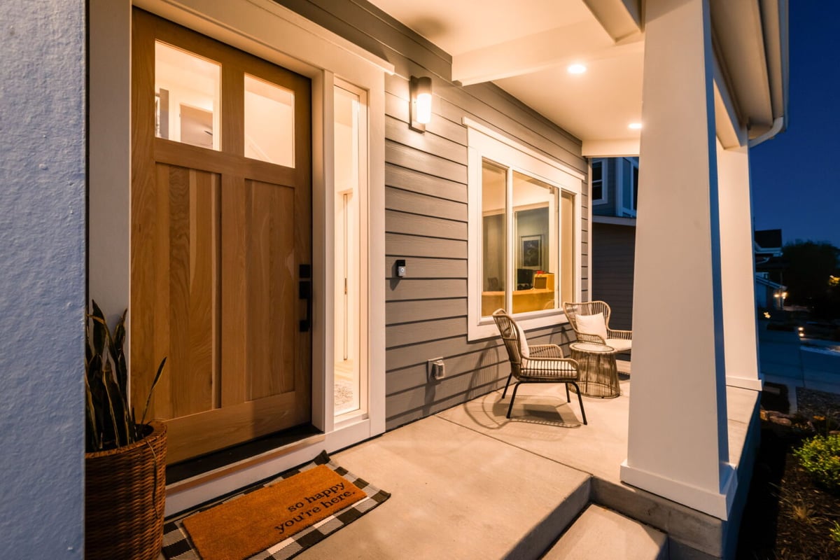 Custom home entry porch at dusk with wood door, seating, and warm lighting in Louisville, CO by Cillessen Construction