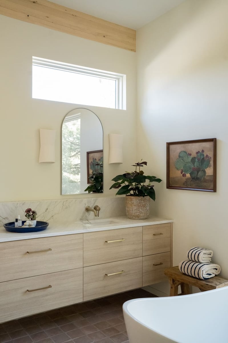 Bathroom vanity with wood cabinets, arched mirror, and plant in Arvada, CO pop top renovation by Cillessen Construction