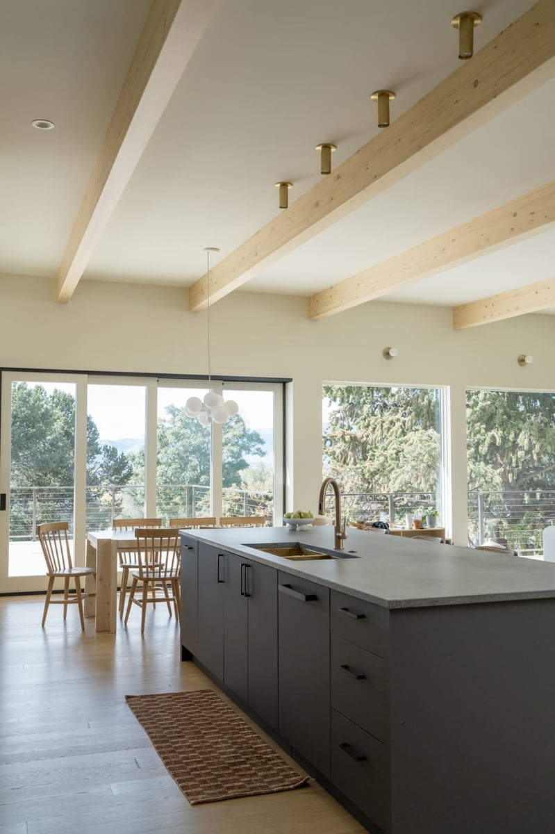 Kitchen island with sink, large windows, and exposed beams in Arvada, CO pop top renovation by Cillessen Construction