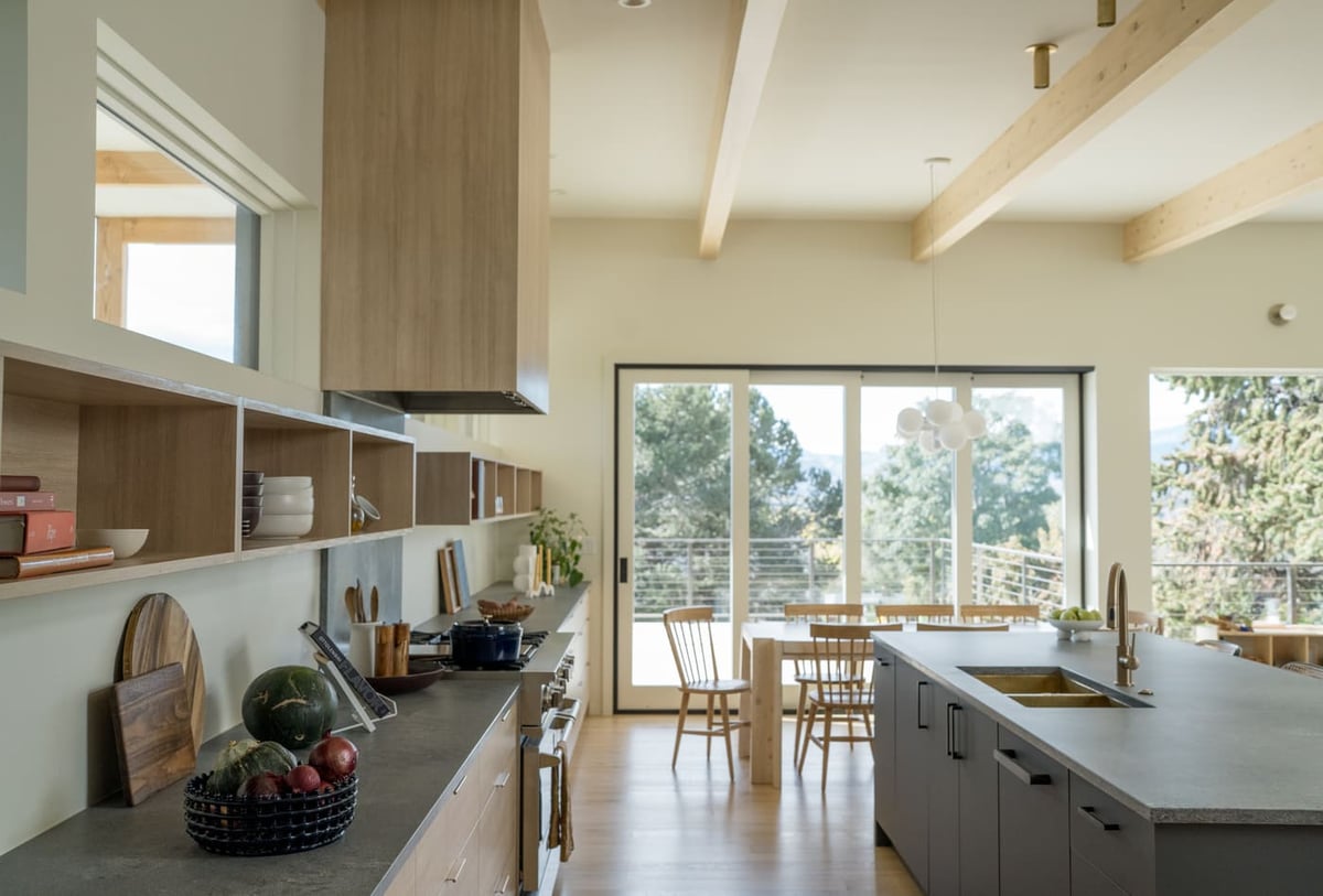 Open kitchen with island, wood cabinetry, and dining area beyond in Arvada, CO pop top renovation by Cillessen Construction