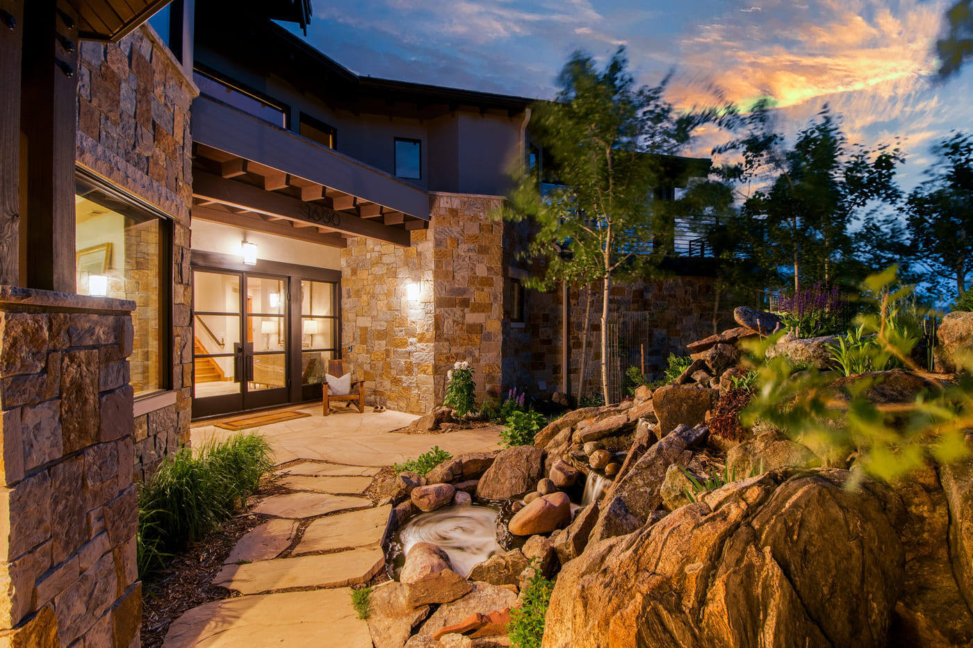 Genesee, CO renovation exterior with stone patio, water feature, and lit entry by Cillessen Construction