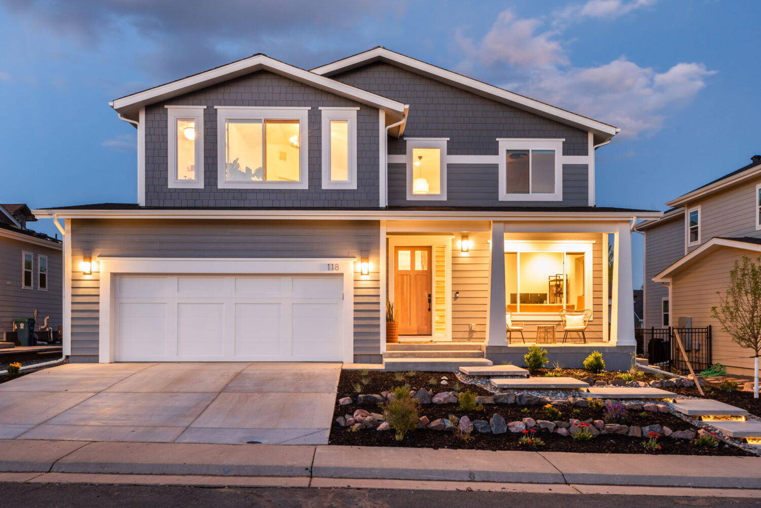 Front exterior of custom home with lit windows, landscaped yard, and covered porch in Louisville, CO by Cillessen Construction